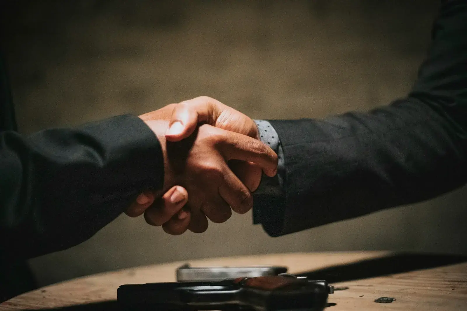 Two people shaking hands over a table after a business negotiation, representing a Joint Business Plan agreement