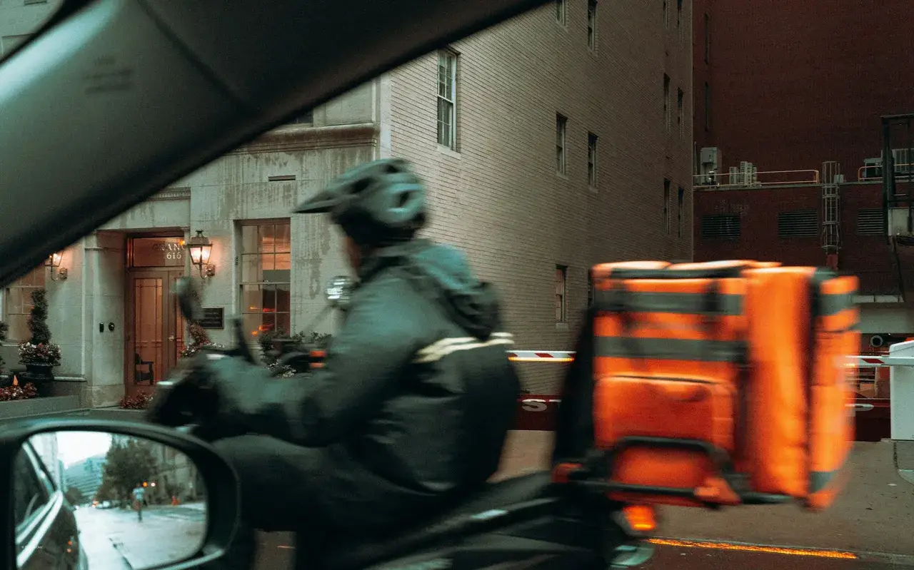 Delivery rider on a scooter with an insulated delivery bag on a city street, representing quick-commerce last-mile delivery